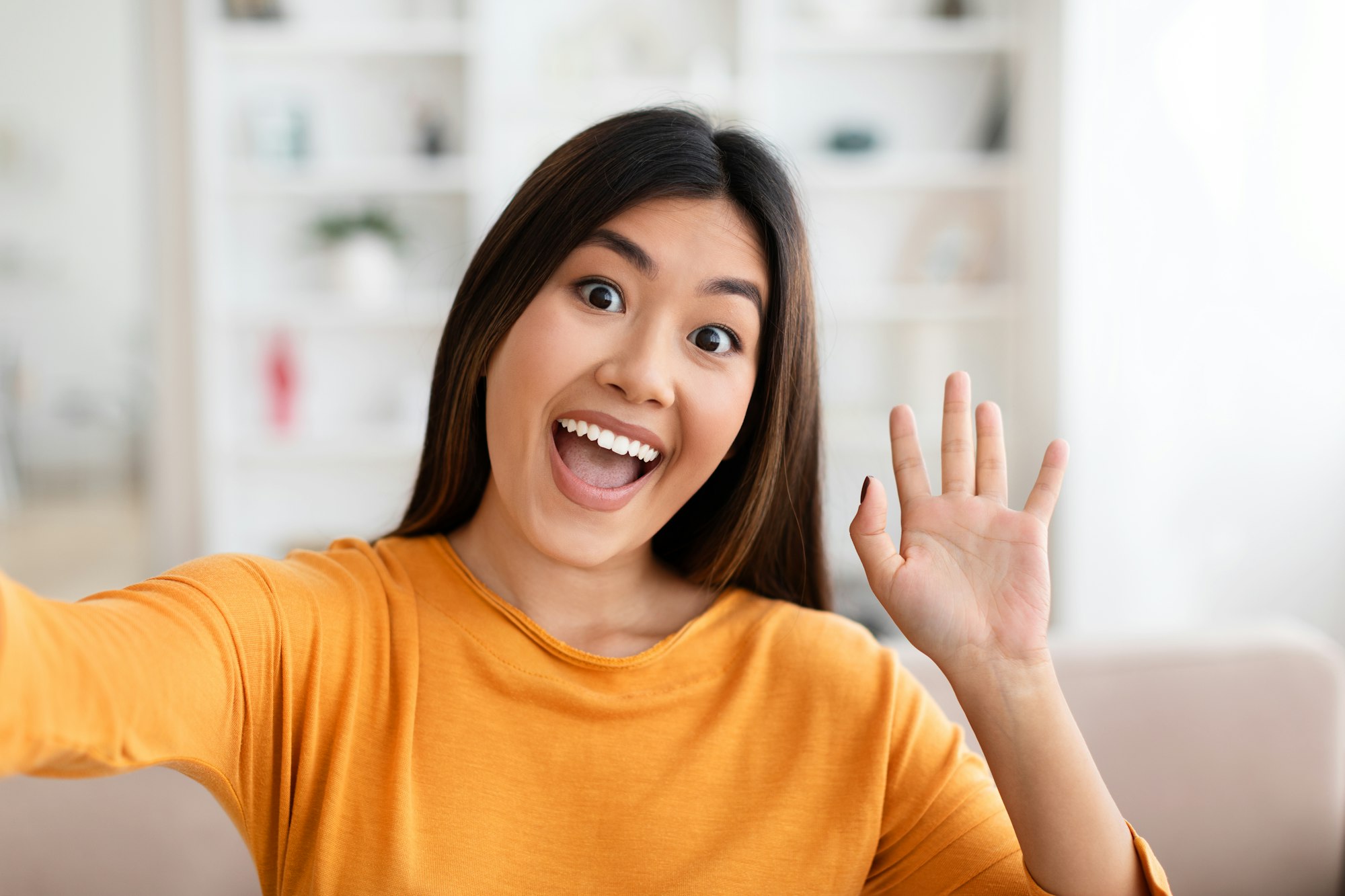 Positive young asian woman taking selfie at home