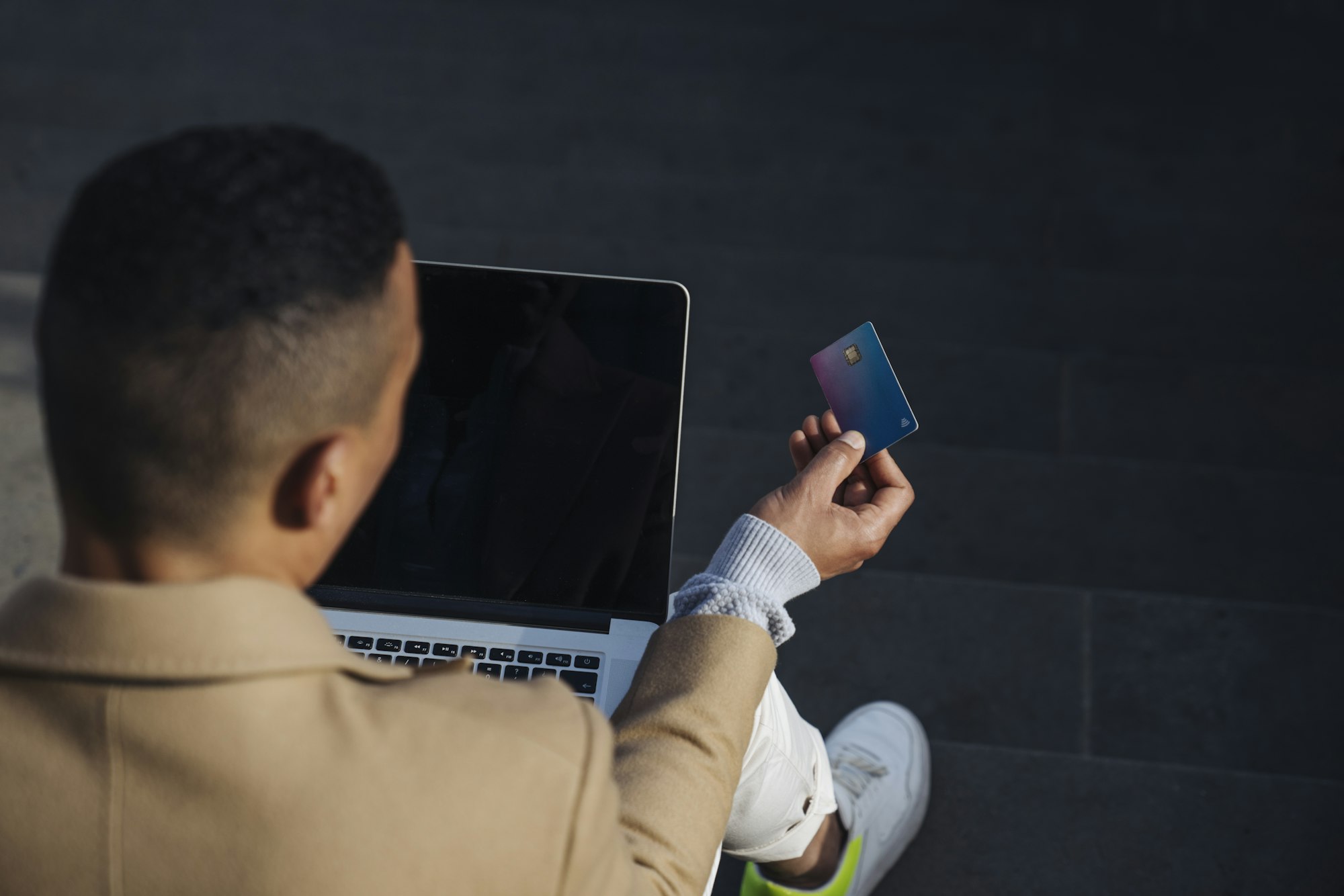 Back view of man sitting outdoors with laptop doing payment with credit card