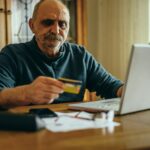 Senior man using a laptop and holding a credit card at home